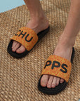 Person wearing orange slides with black text on a woven mat