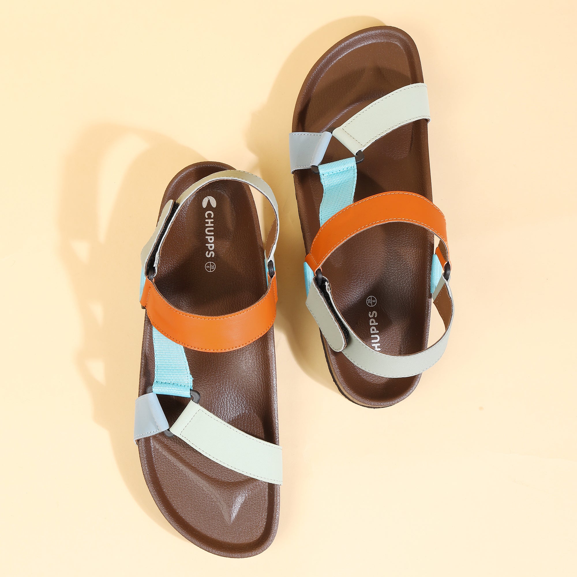 Pair of sandals with brown leather and colorful straps on a beige background