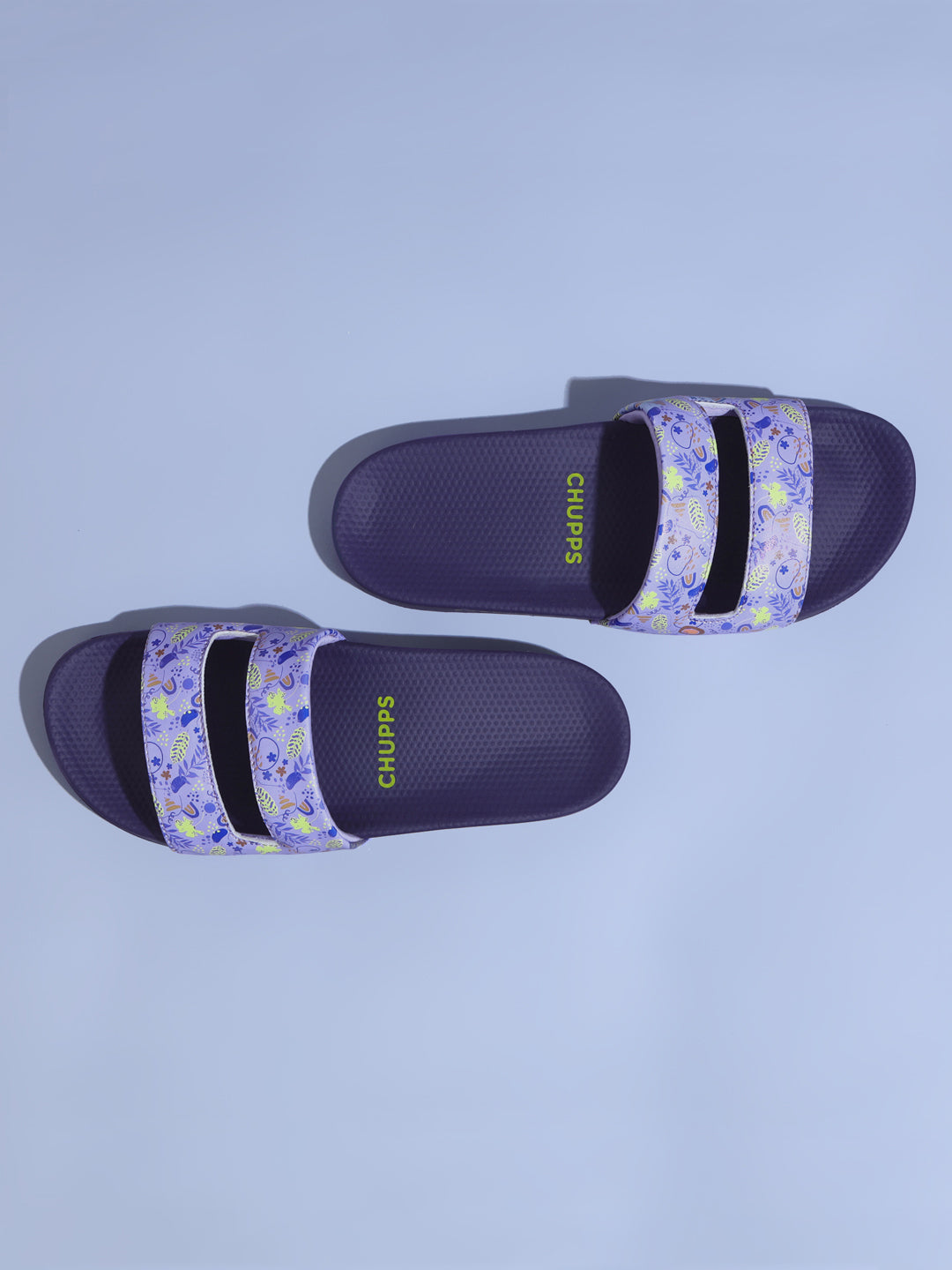 Pair of Mimo purple slides with floral straps on a light blue background