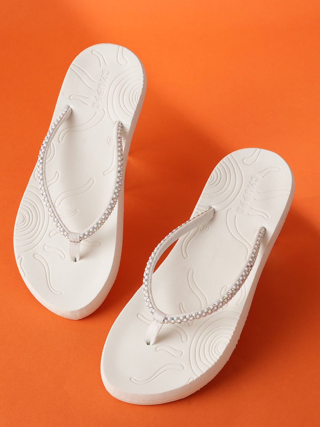 Top-down view of Chupps Solis pair with glitter-detailed V-straps and soft footbed on an orange background