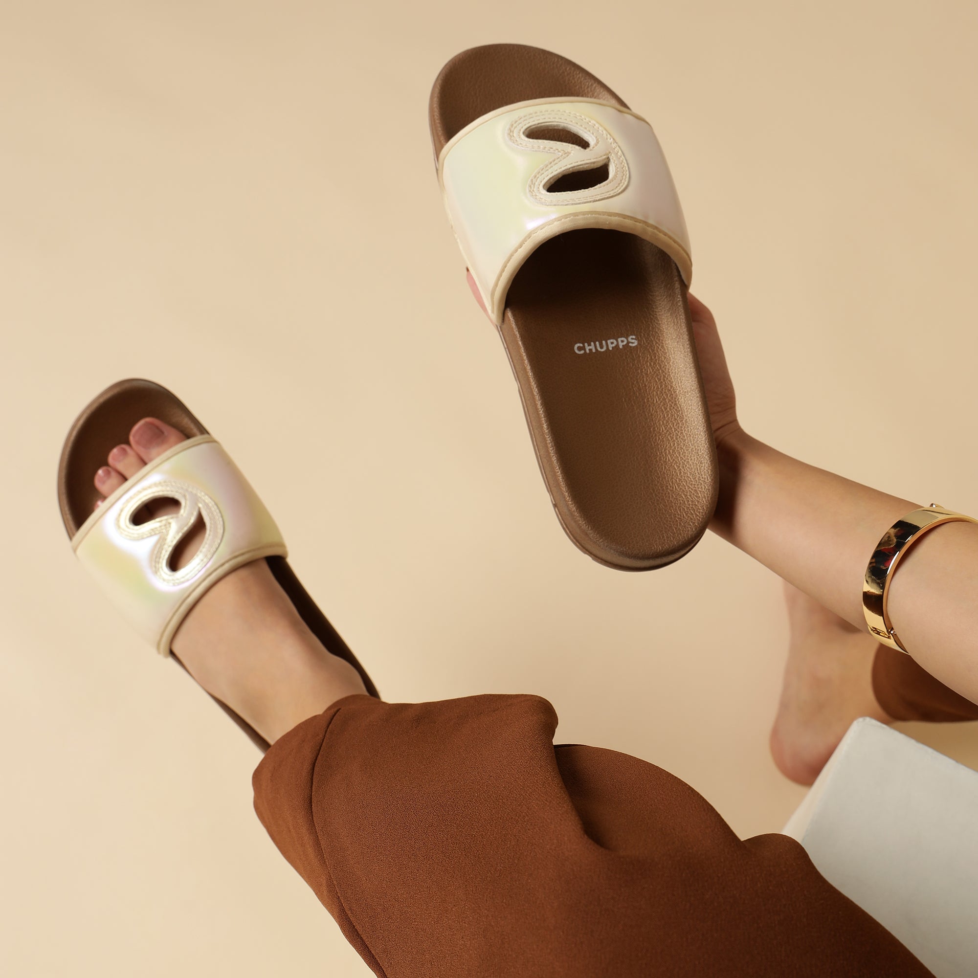 Person wearing beige slides with brown soles on a beige background