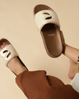 Person wearing beige slides with brown soles on a beige background