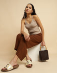 Woman sitting on a white stool holding a brown handbag against a beige background