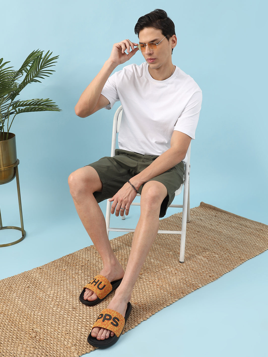 Man sitting on a chair wearing a white t-shirt, green shorts, and orange slides with a blue background